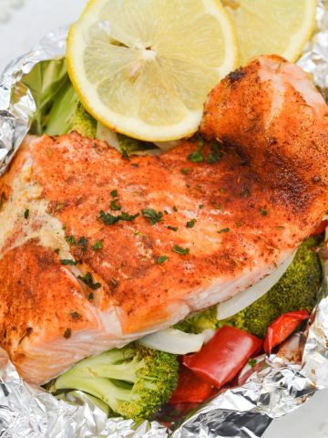 Blackened salmon wrapped in foil with vegetables on a plate.
