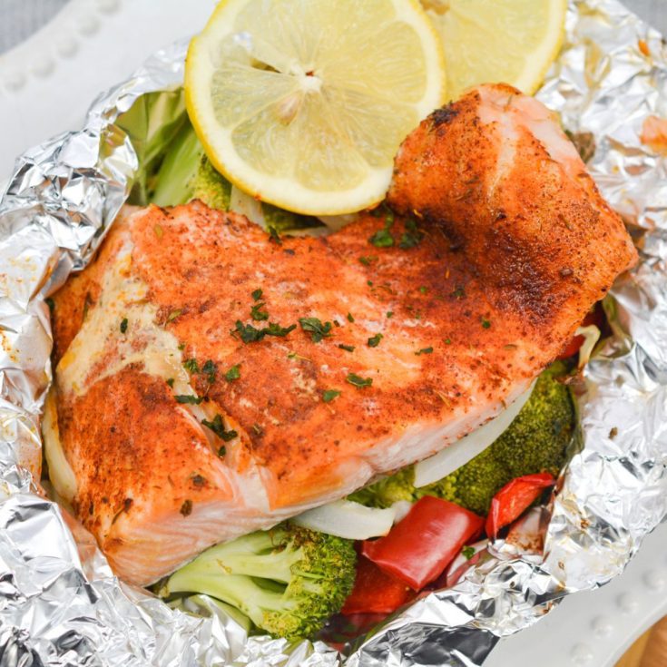 Blackened salmon wrapped in foil with vegetables on a plate.