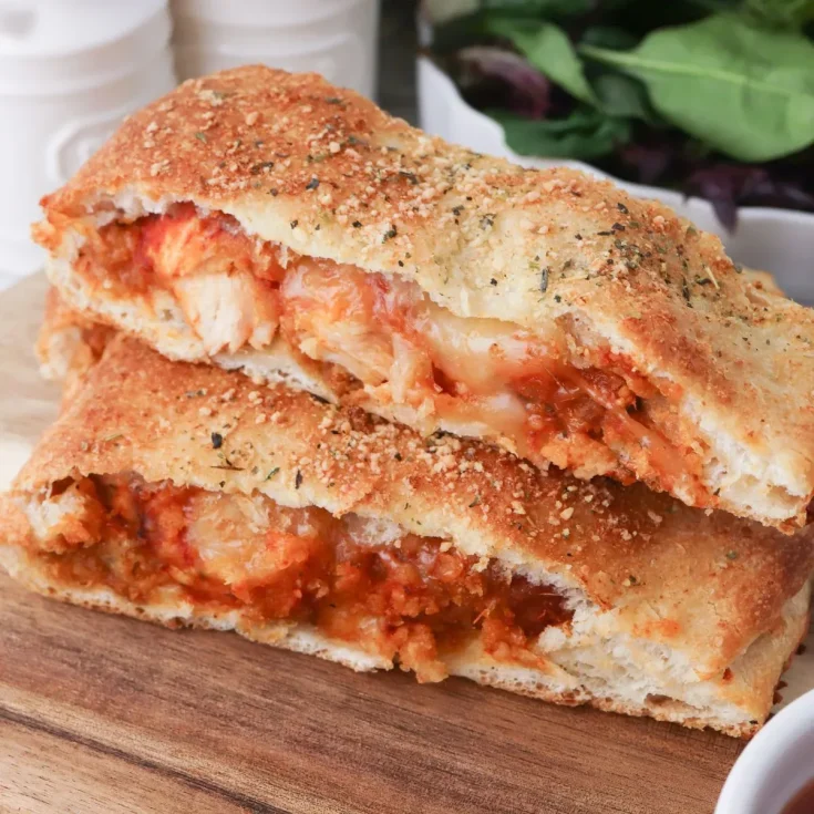 Chicken parmigiana pizza on a wooden cutting board.