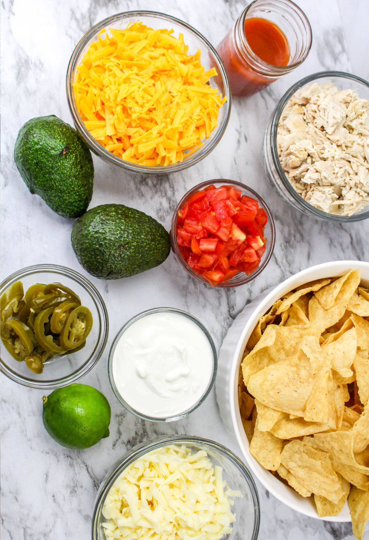 The ingredients for chicken nachos are laid out on a marble countertop.