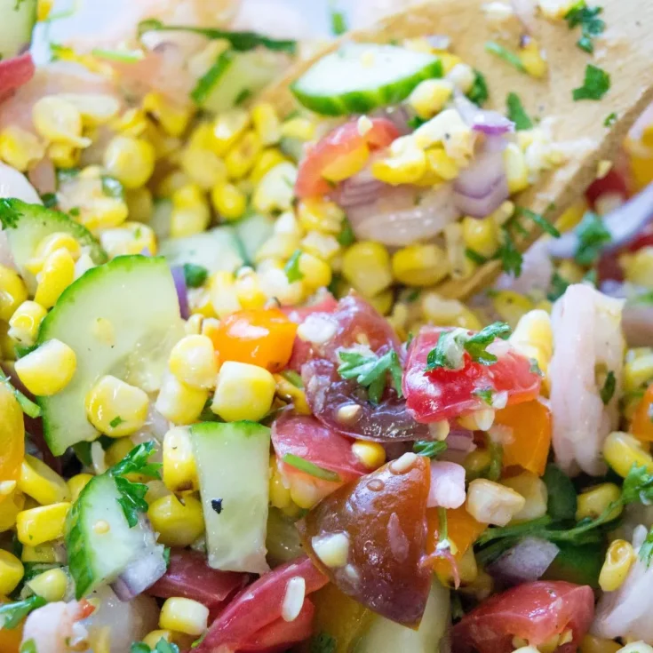 A bowl of corn and cucumber salad with a wooden spoon.