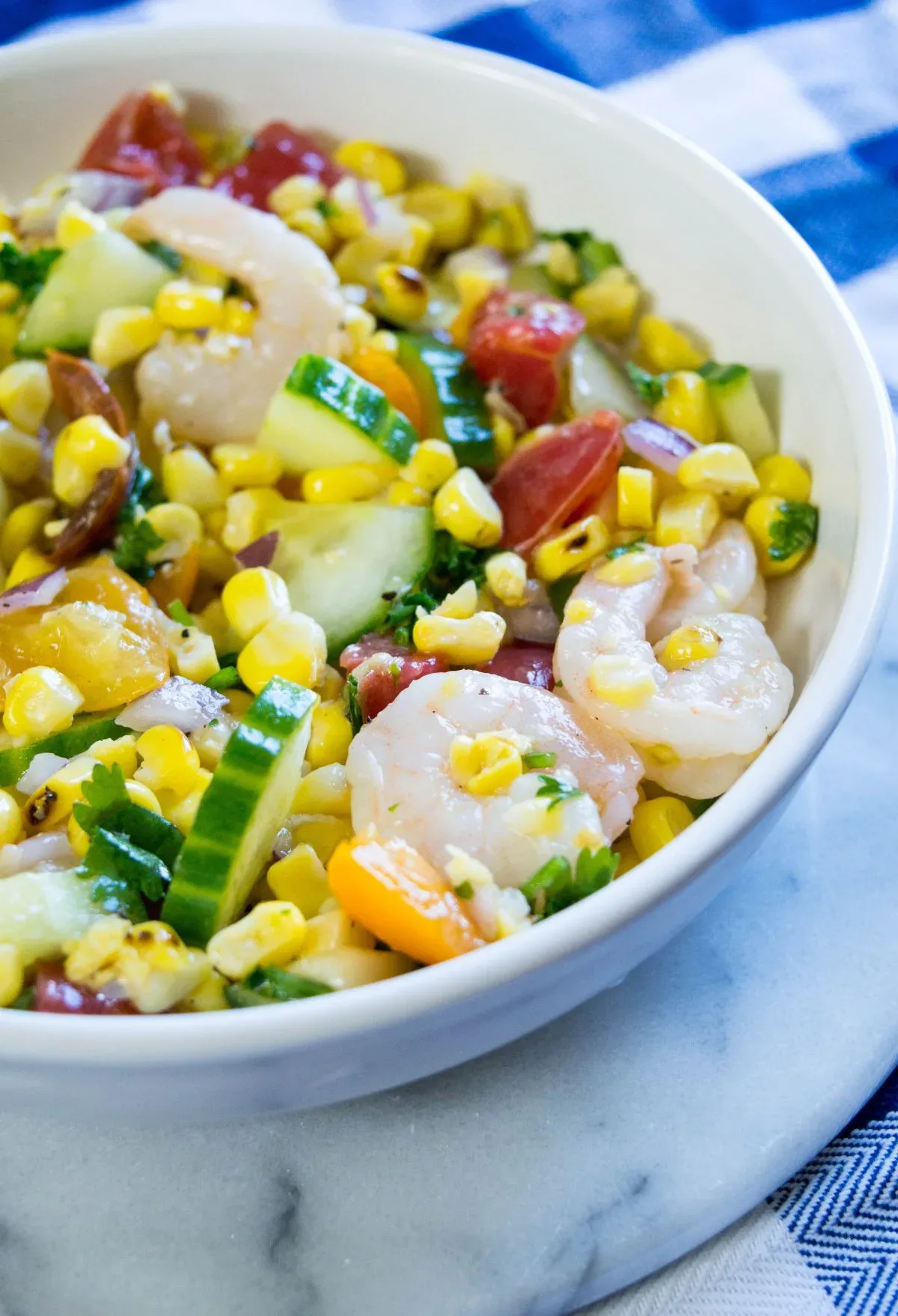 A white bowl with shrimp, corn, tomatoes and cucumbers.