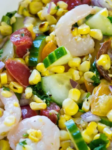 A white bowl with shrimp, corn, tomatoes and cucumbers.