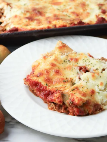 Lasagna on a plate with bread on the side.