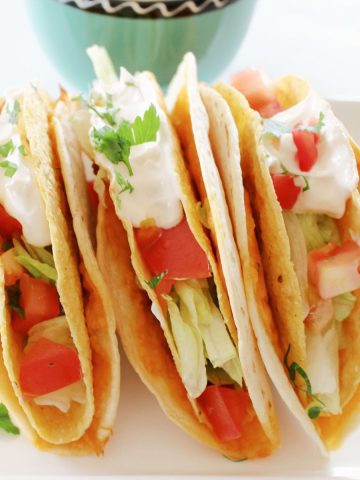 Cheesy Mexican tacos with sour cream on a white plate.
