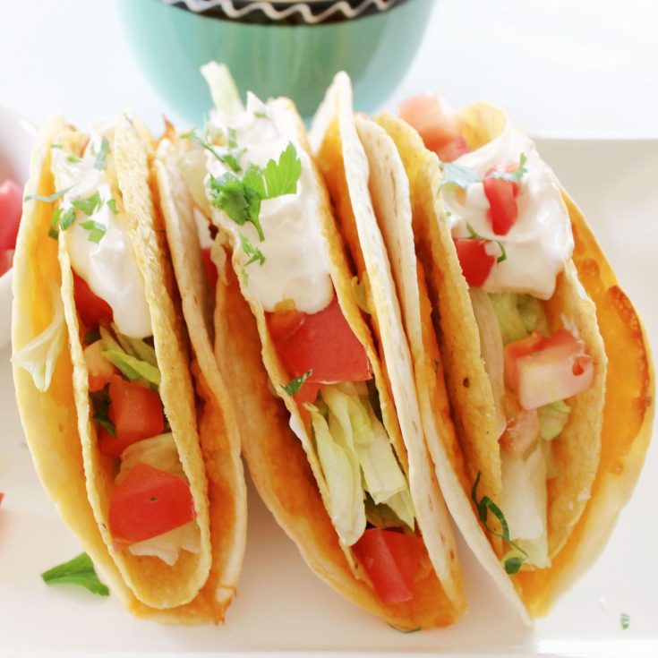 Cheesy Mexican tacos with sour cream on a white plate.