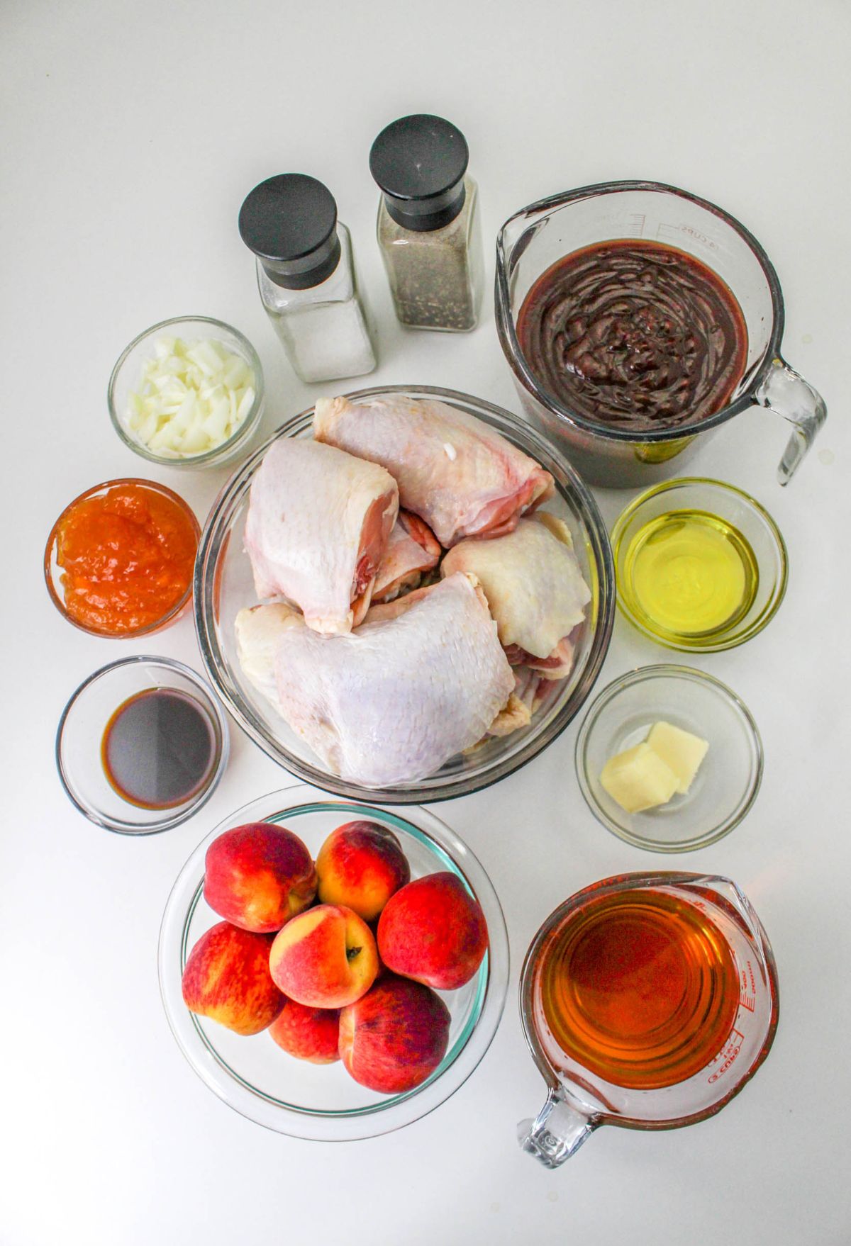 The ingredients for a chicken dish are laid out on a white surface, including peaches.