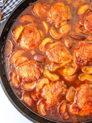 Peach whiskey chicken cooked in a skillet with juicy peaches.