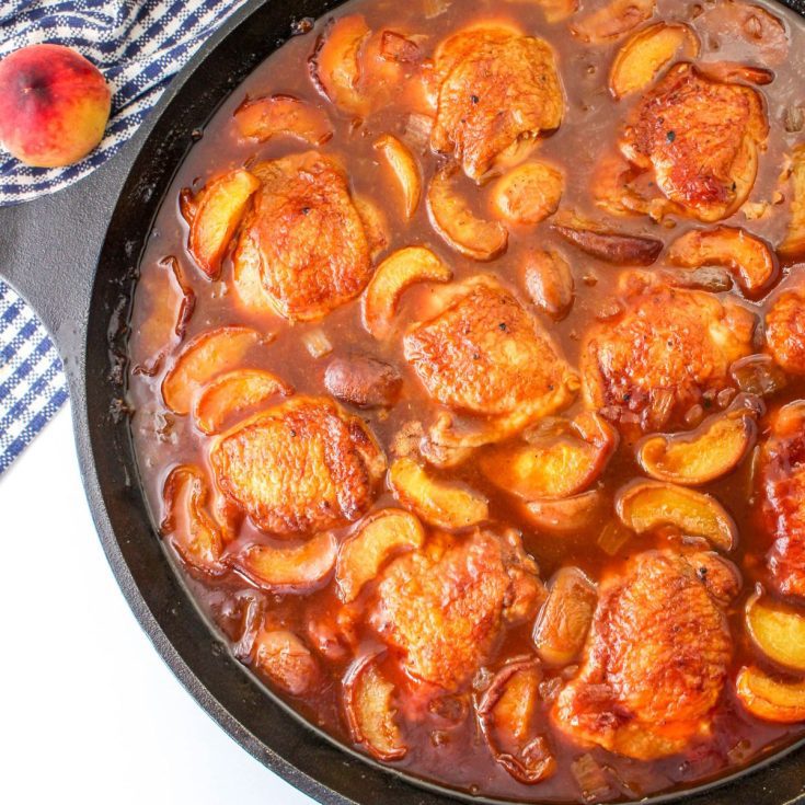 Peach whiskey chicken cooked in a skillet with juicy peaches.