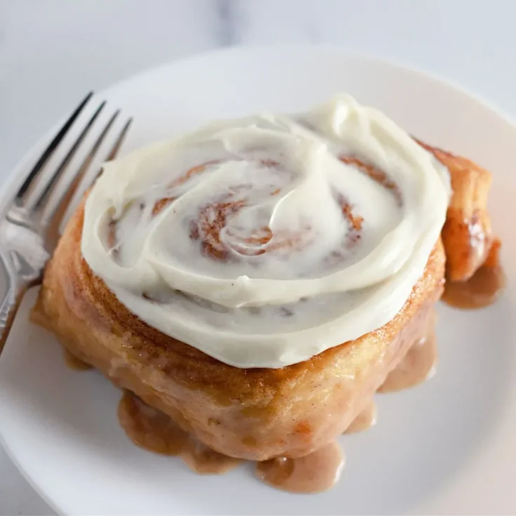 A cinnamon roll with icing and a fork on a plate.
