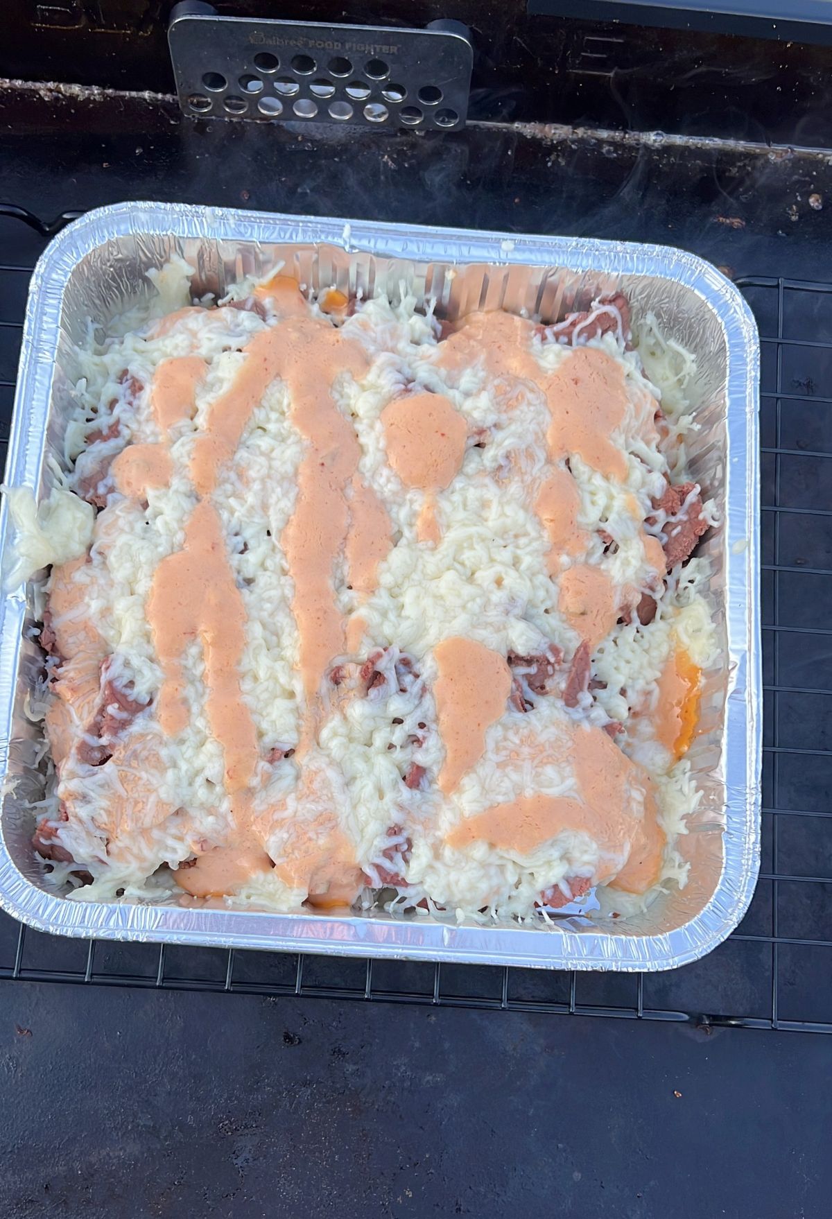 A casserole dish with cheese and sauce sitting on top of a grill.