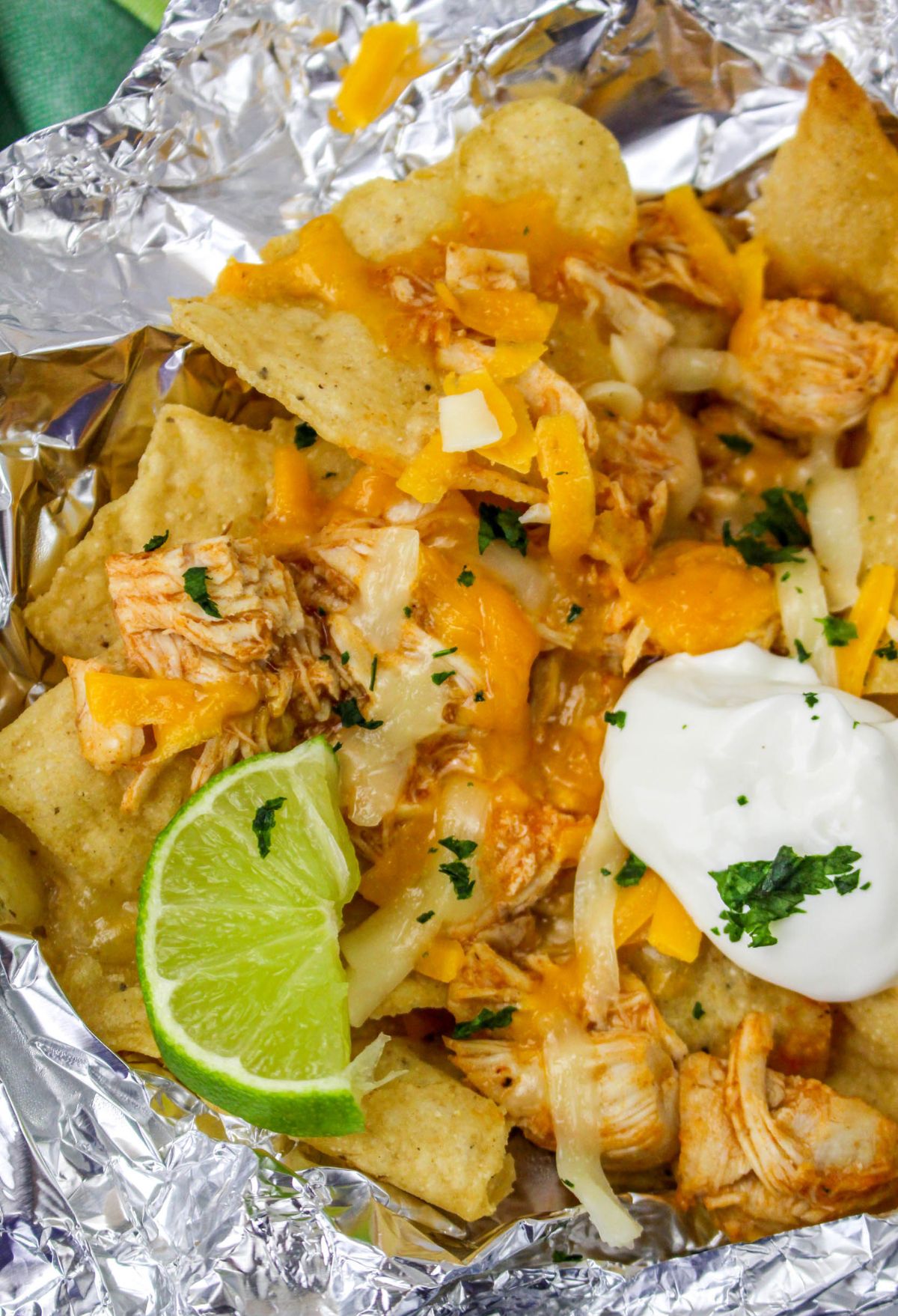 Chicken nachos in foil with sour cream and lime wedges make for a delicious and satisfying meal.